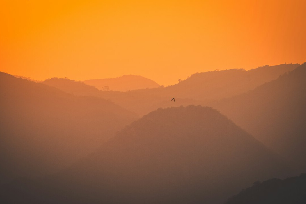 Warm orange sunrise over mountains with a small silhouette of a person